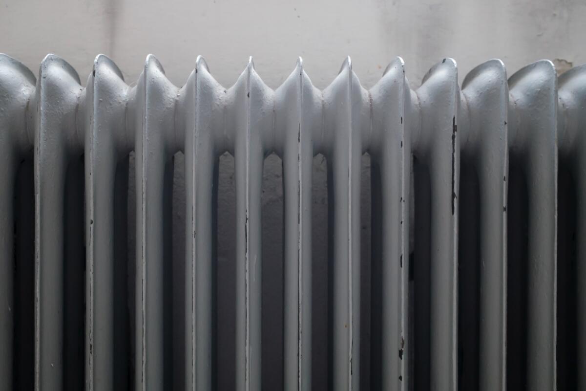 Old cast-iron radiator, painted grey, with peeling paint, against the wall. Close-up.